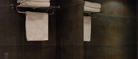 A modern bathroom with a large mirror, dark tiled walls, a white sink, and two towel racks with folded towels.