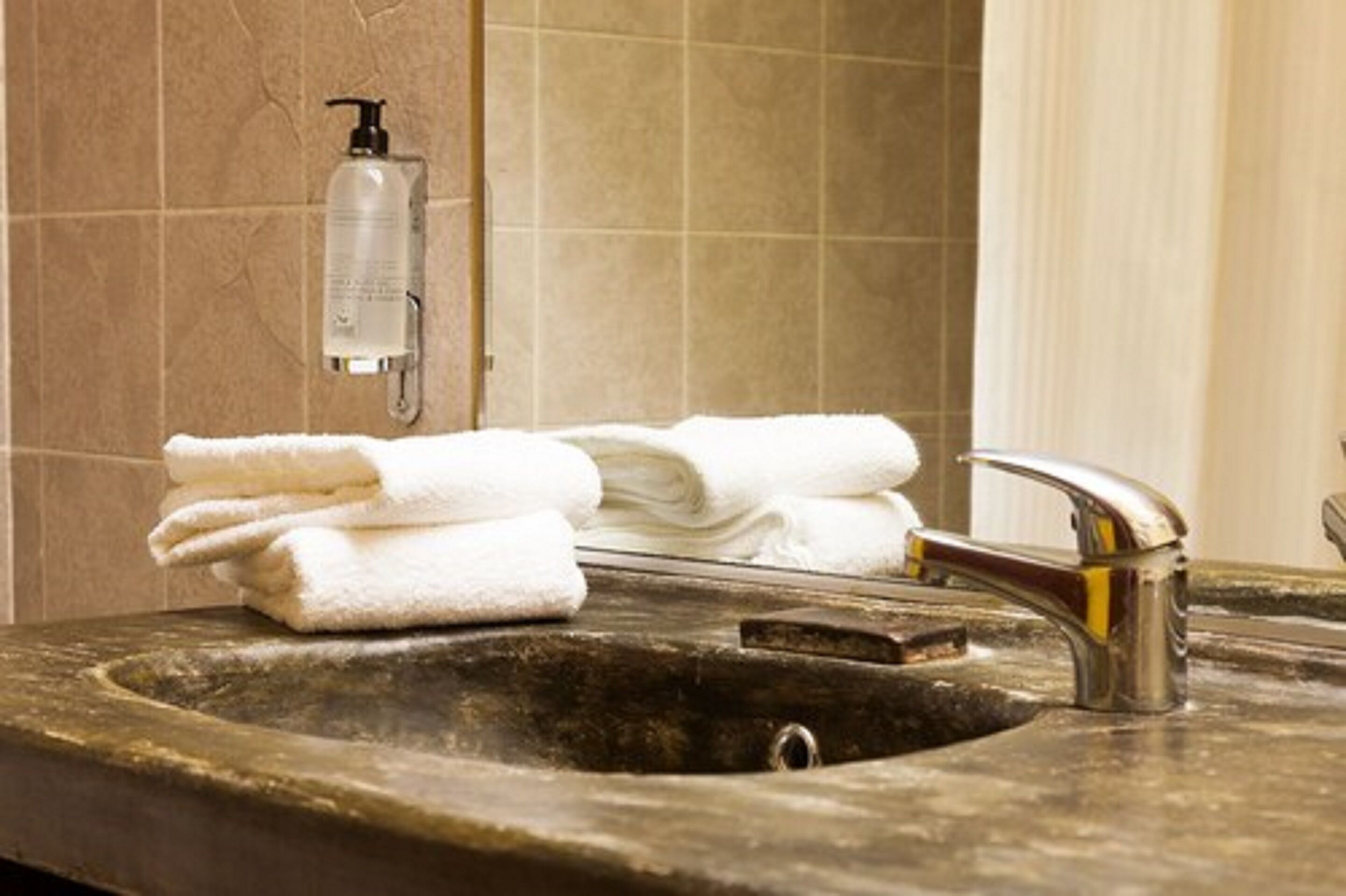 A bathroom sink with a towel stack, a soap dispenser, and a mirror.