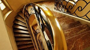 A spiral staircase with a golden handrail and black balusters, leading to a landing with a marble floor. - Du Soleil Le Terminus (Carcassonne)