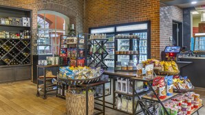 Una tienda de paredes de ladrillo con estantes llenos de aperitivos, bebidas y una selección de vinos.
