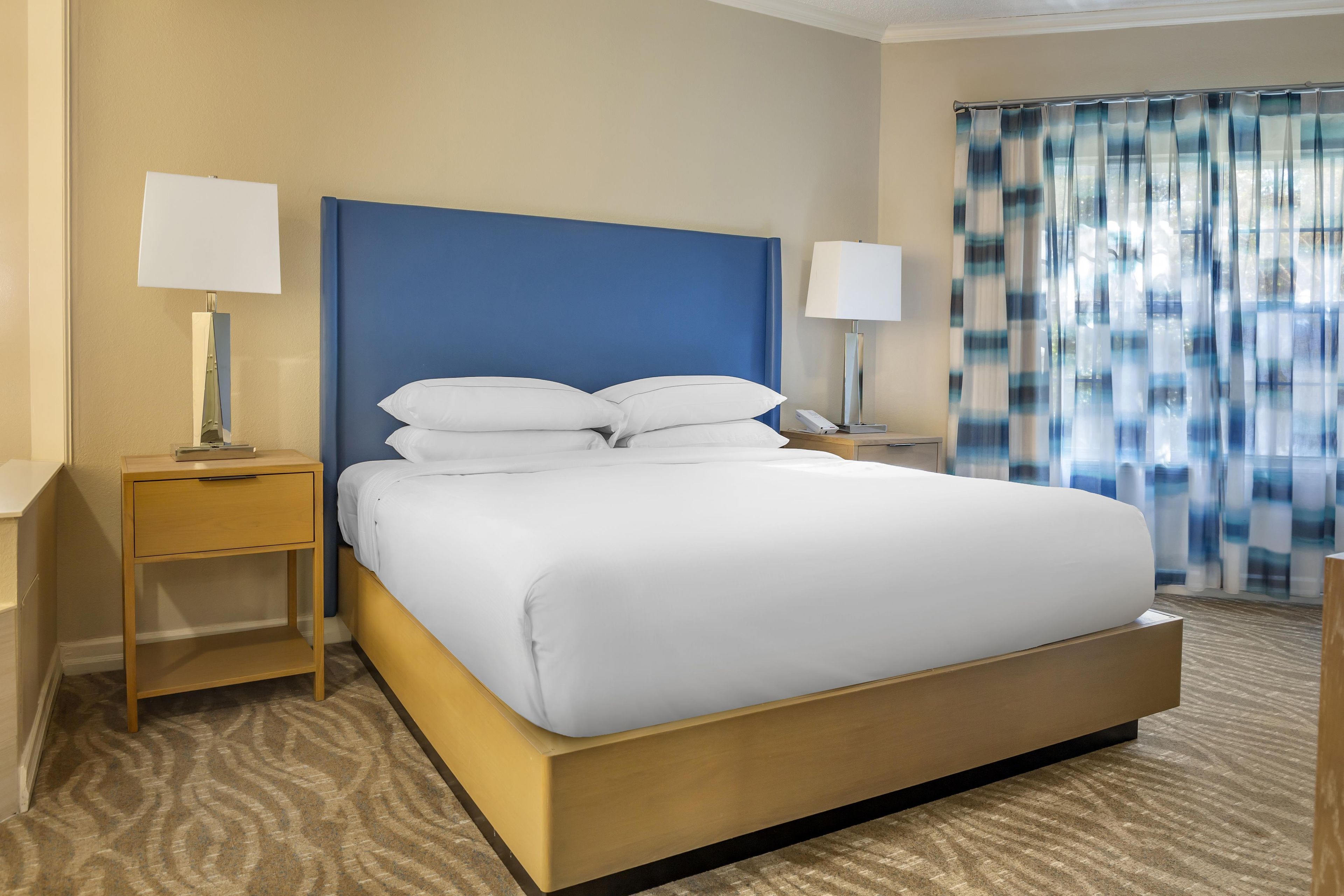 A hotel room with a large bed, two bedside tables, and a window with curtains.