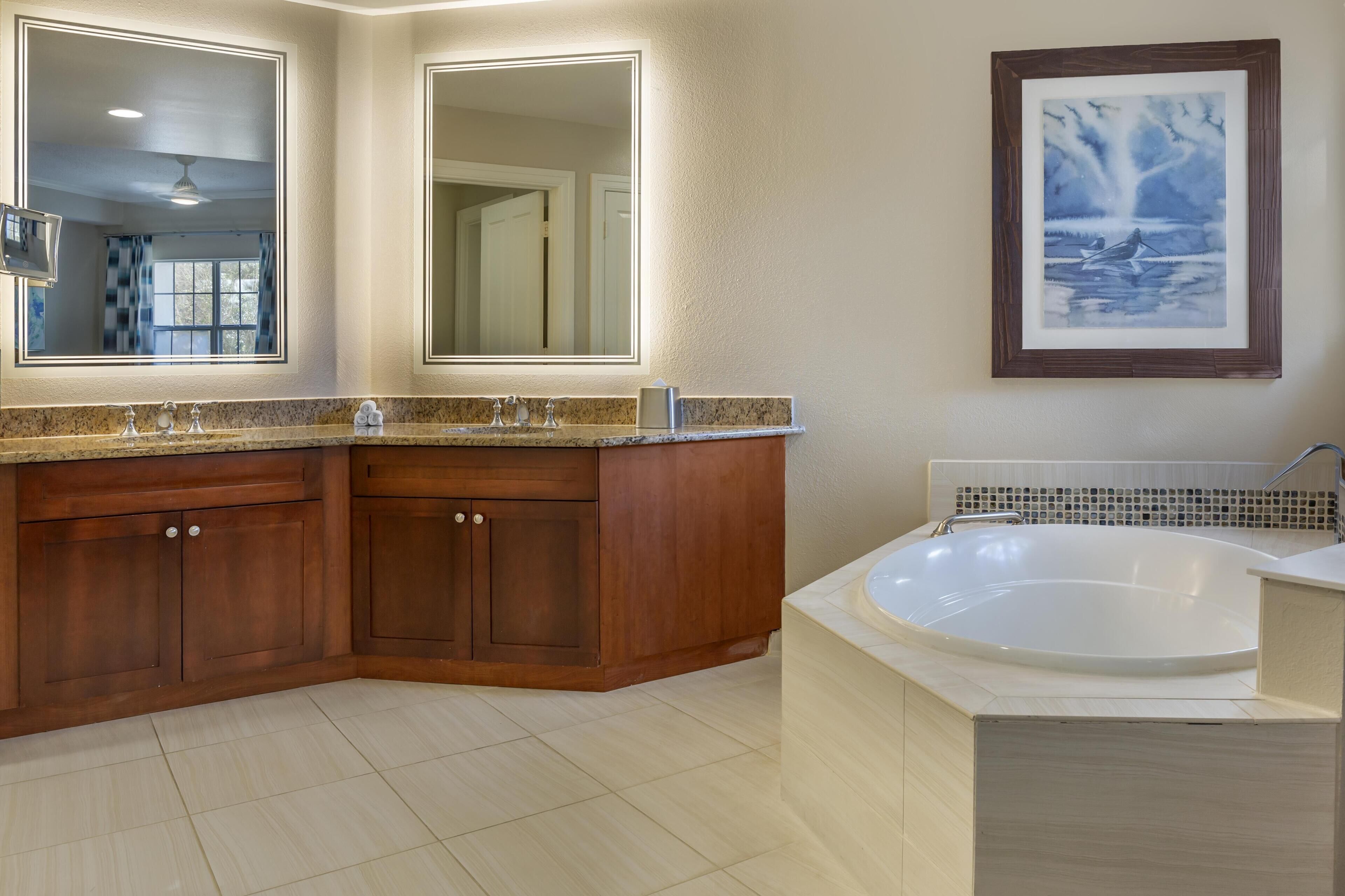 Un baño con un espejo grande, una bañera y armarios de madera.