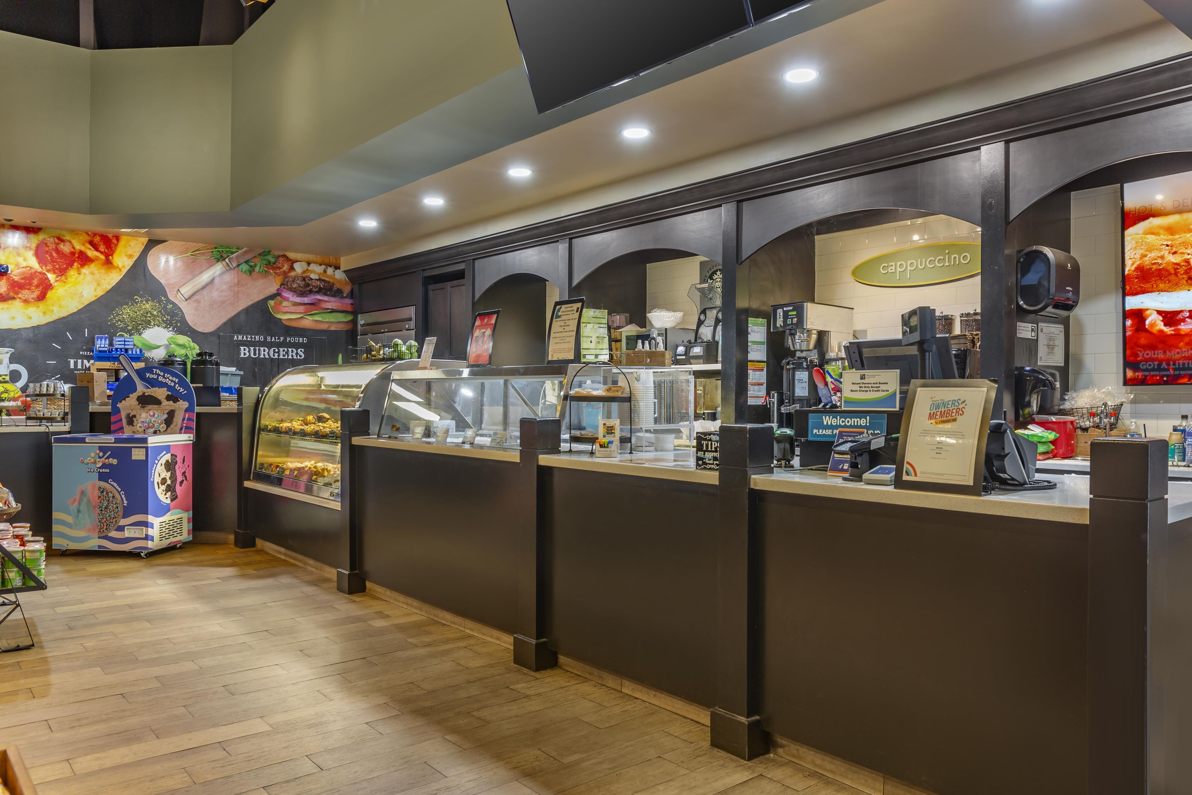 Un patio de comidas con diversas opciones de comida, incluyendo una exposición de hamburguesas y una estación de cappuccino.