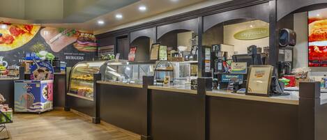 Un patio de comidas con diversas opciones de comida, incluyendo una exposición de hamburguesas y una estación de cappuccino.