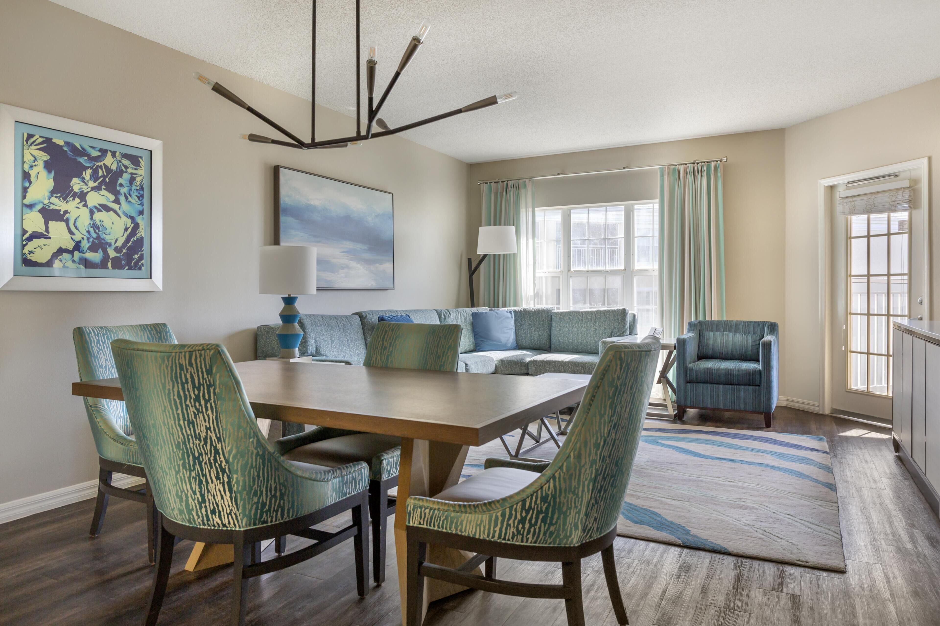 A dining area with a wooden table and chairs, a sofa set, and a chandelier.