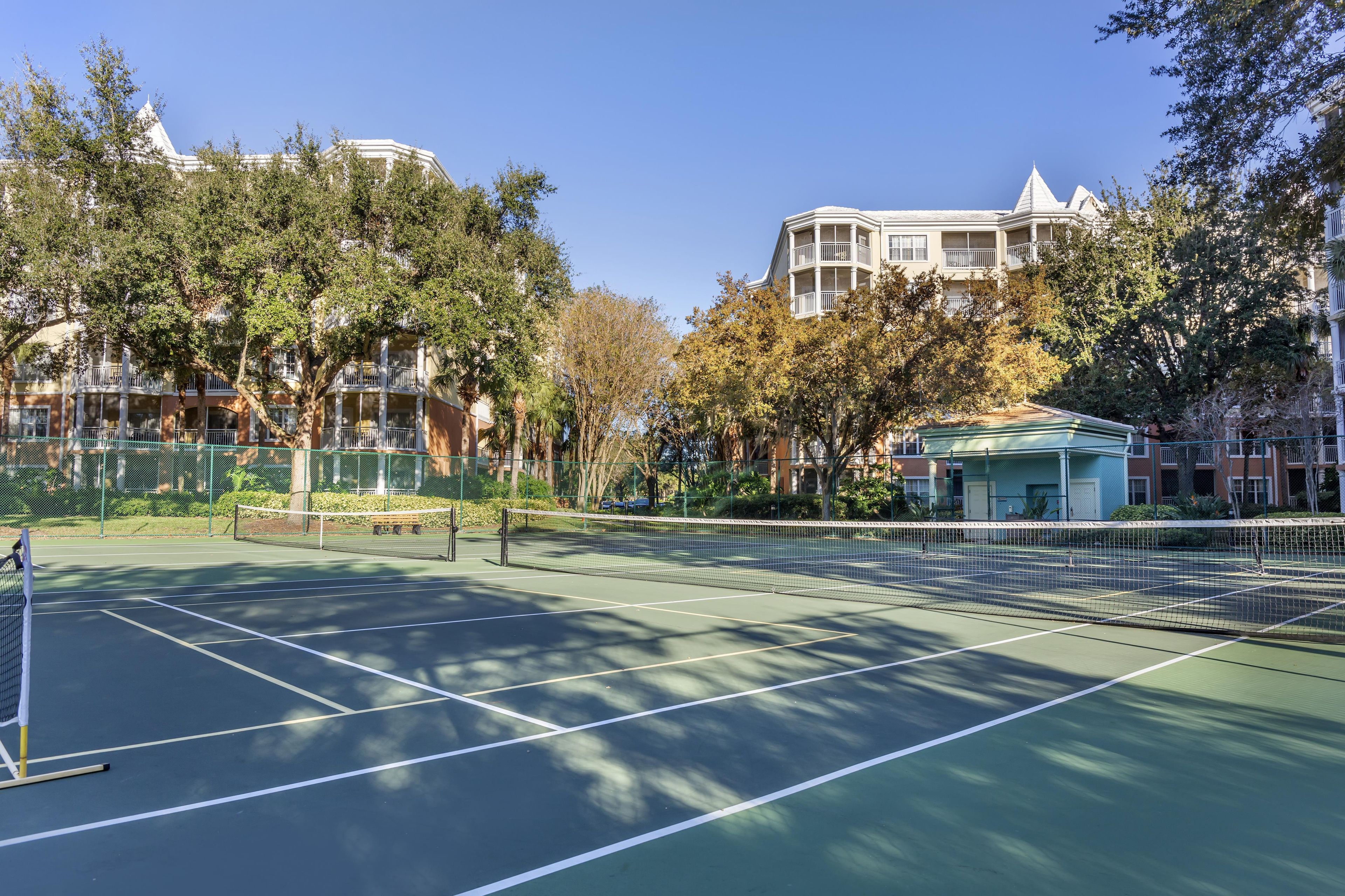 Una cancha de tenis con red, rodeada de árboles y edificios.