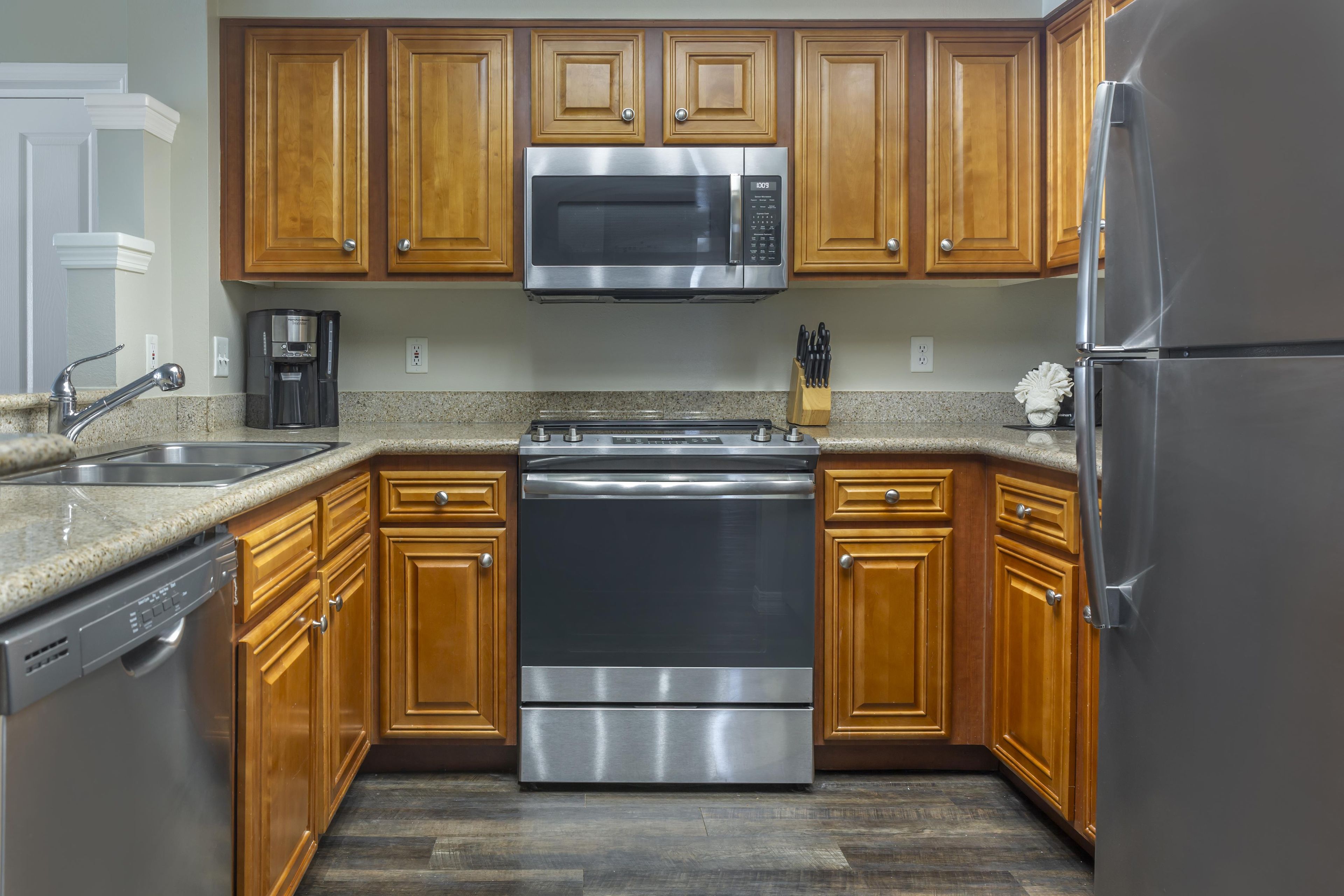 A kitchen with wooden cabinets, stainless steel appliances including a microwave, stove, and refrigerator, and a granite countertop.