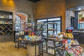 Interior de una tienda con estantes llenos de bocadillos, una sección refrigerada y una exhibición de vinos.