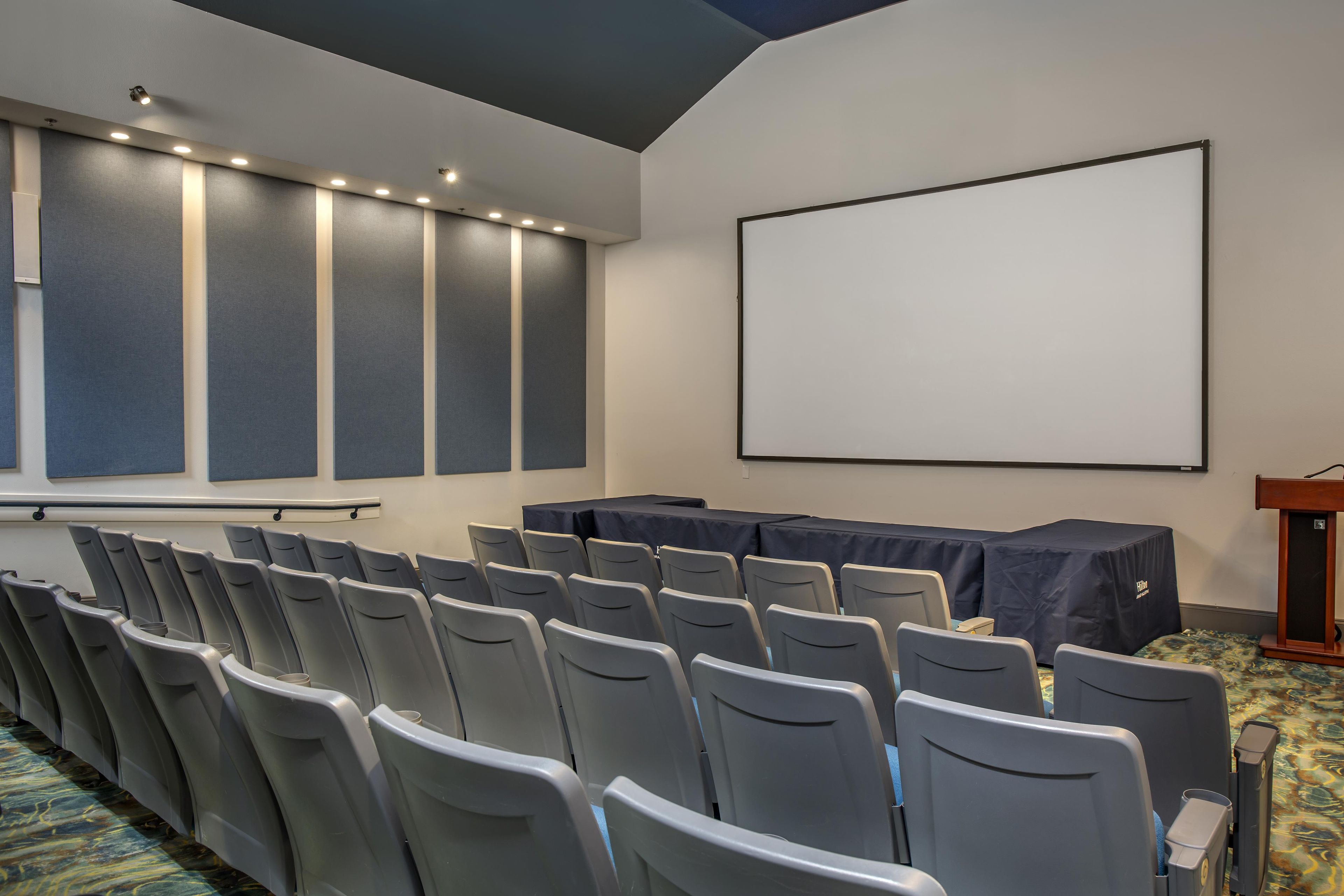 A conference room with rows of chairs, a projector screen, and a podium.