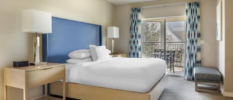 A hotel room with a bed, bedside tables, a desk, a chair, and a balcony with curtains.