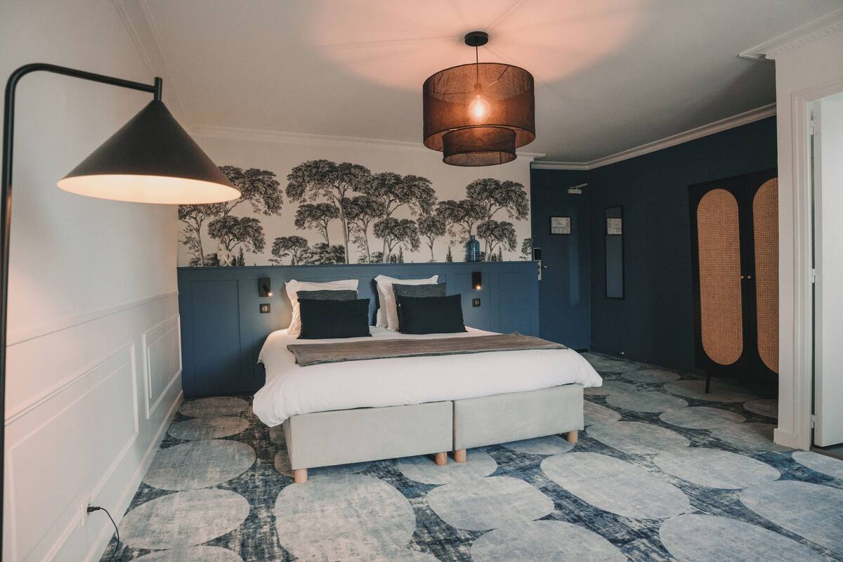 A bedroom with a bed, a hanging lamp, a wall-mounted light, and a patterned carpet.