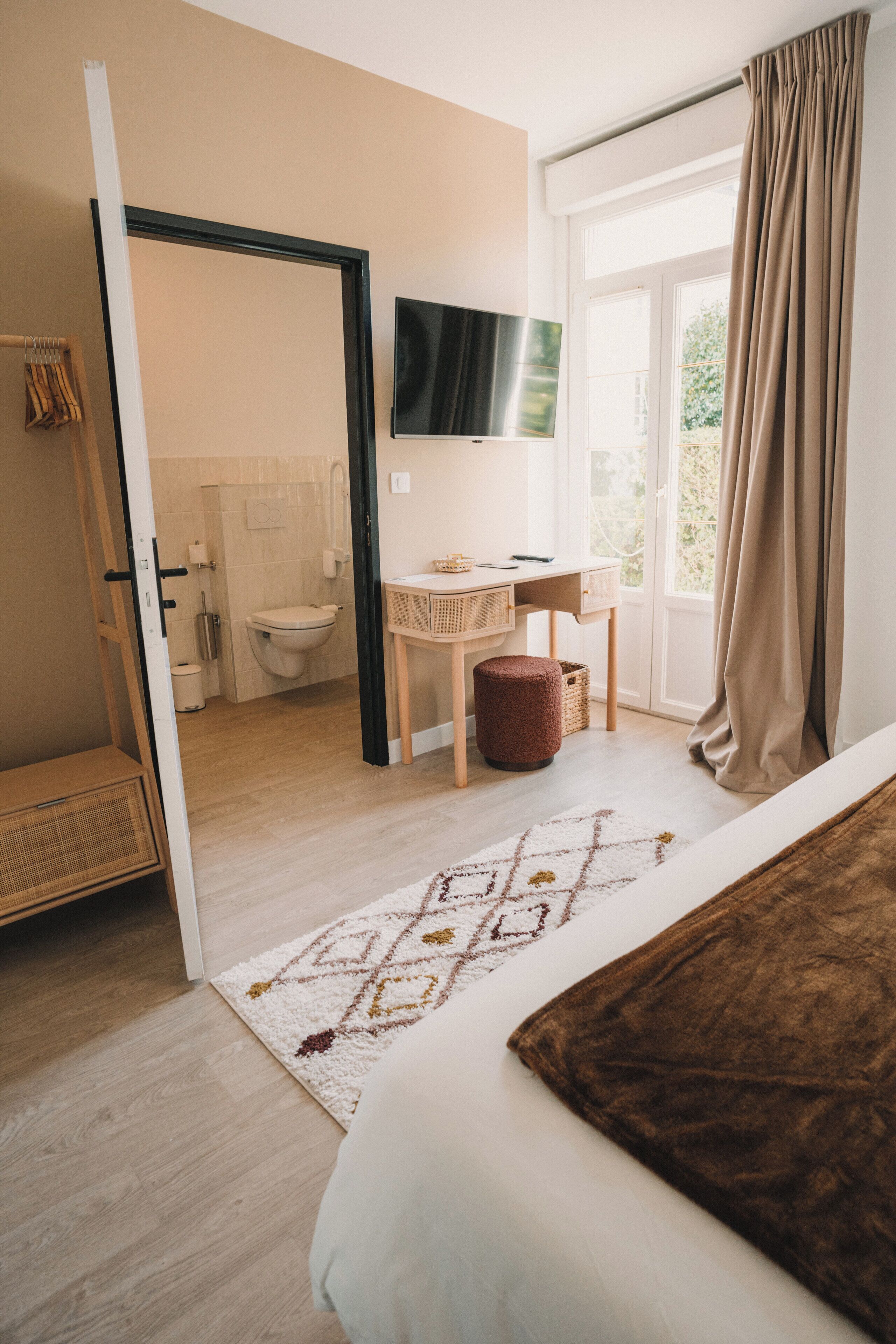Une chambre à coucher comprenant un lit, un bureau, une chaise, un téléviseur et une salle de bain visible à travers une porte ouverte.