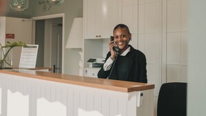 Een receptiebalie met een houten aanrecht en een persoon aan de telefoon. Boven de balie hangen hanglampen.
