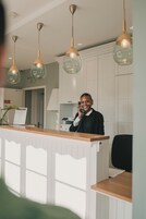 Un comptoir d’accueil avec un plan de travail en bois et une personne au téléphone. Des lampes suspendues sont fixées au-dessus du comptoir.