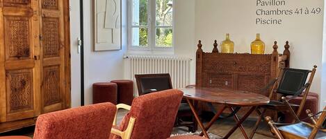A room with a wooden cabinet, a table, and red upholstered chairs. There is a window with a view of trees outside.