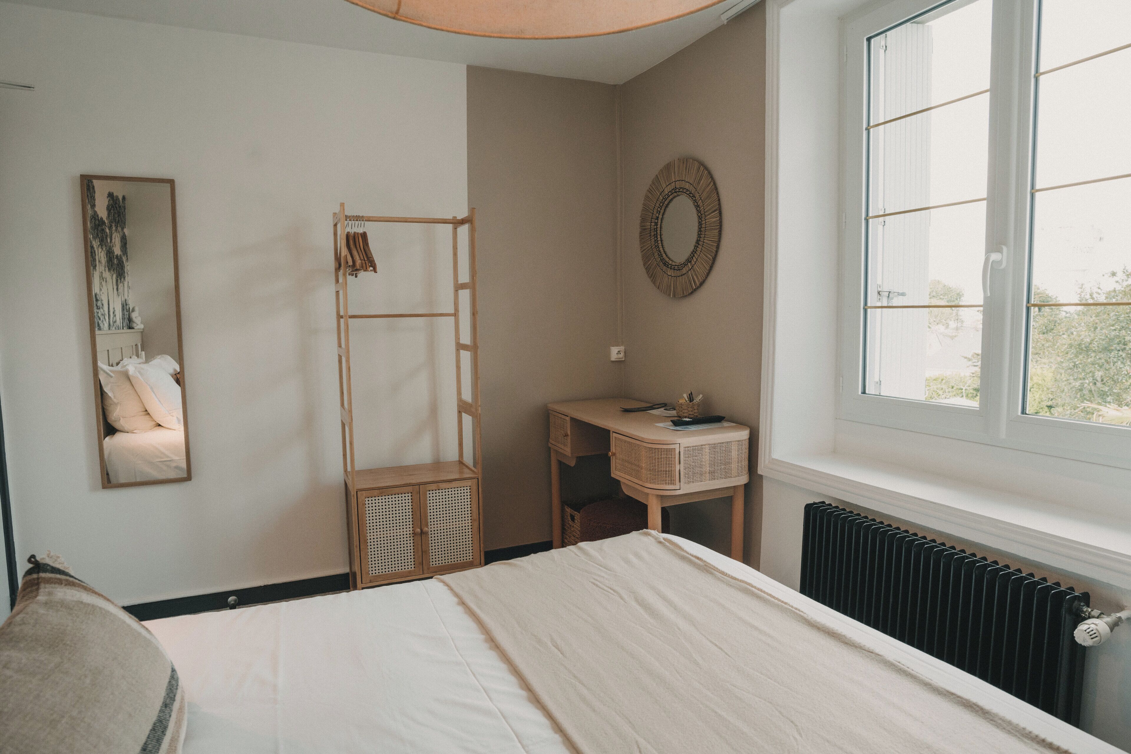 Un dormitorio con cama, armario de madera, una mesita de noche con espejo y ventana con vistas.