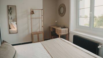 Un dormitorio con cama, armario de madera, una mesita de noche con espejo y ventana con vistas.