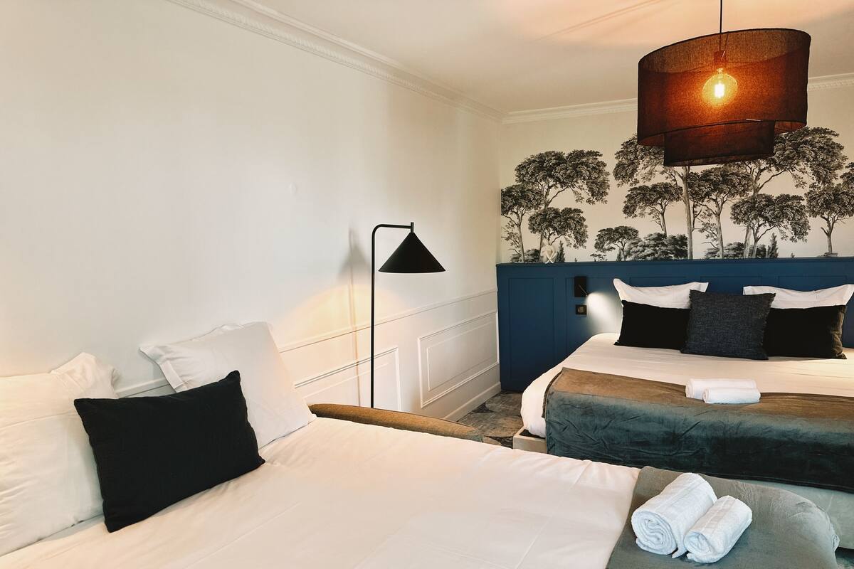 A hotel room with two beds, a blue headboard, a wall mural, and a floor lamp.