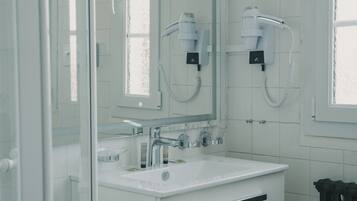 A modern bathroom with a glass shower enclosure, a white sink with a mirror above it, and a hairdryer mounted on the wall.