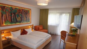 A hotel room with a bed, a desk, a chair, a television, a painting on the wall, and a window with curtains.