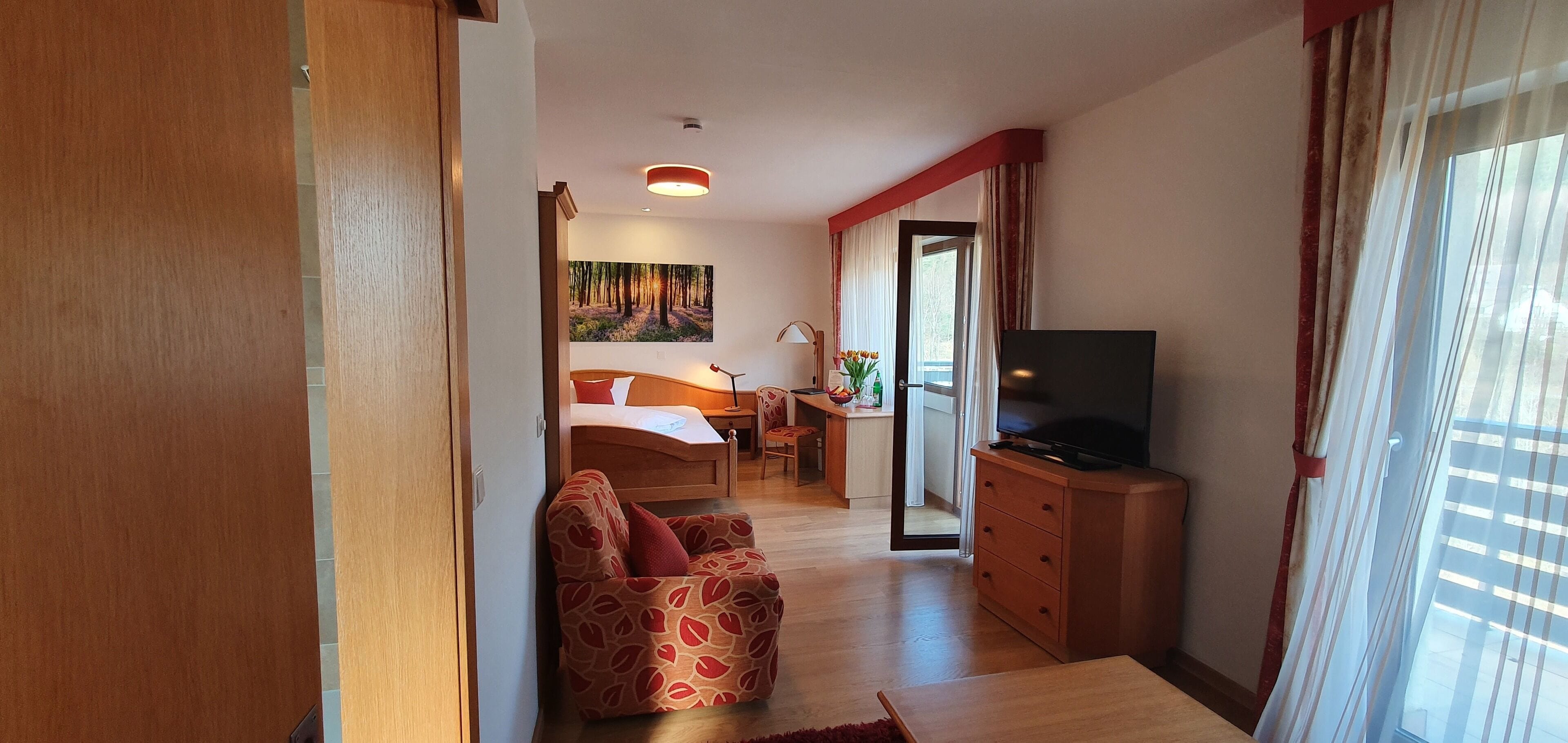 Ein Hotelzimmer mit Bett, Schreibtisch, Sessel, Fernseher und einem Gemälde an der Wand.