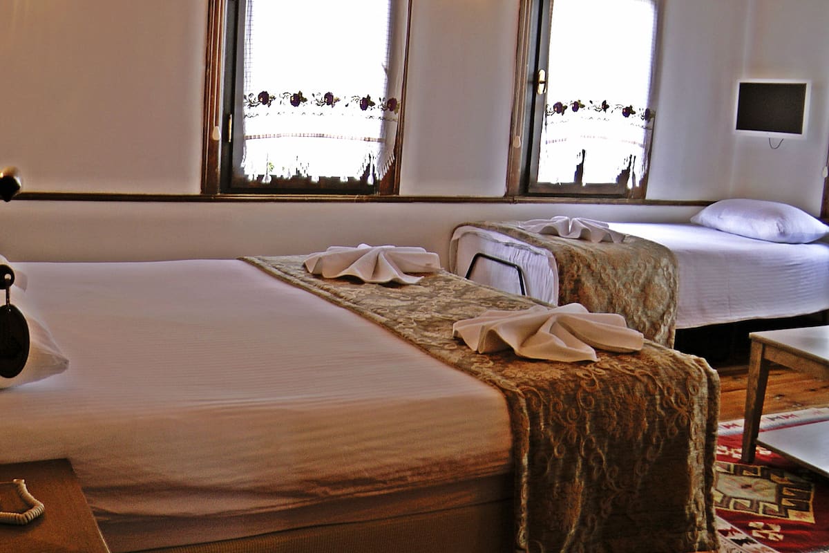 Habitación de hotel con dos camas, suelo de madera, una mesita y ventana con vista a la calle.
