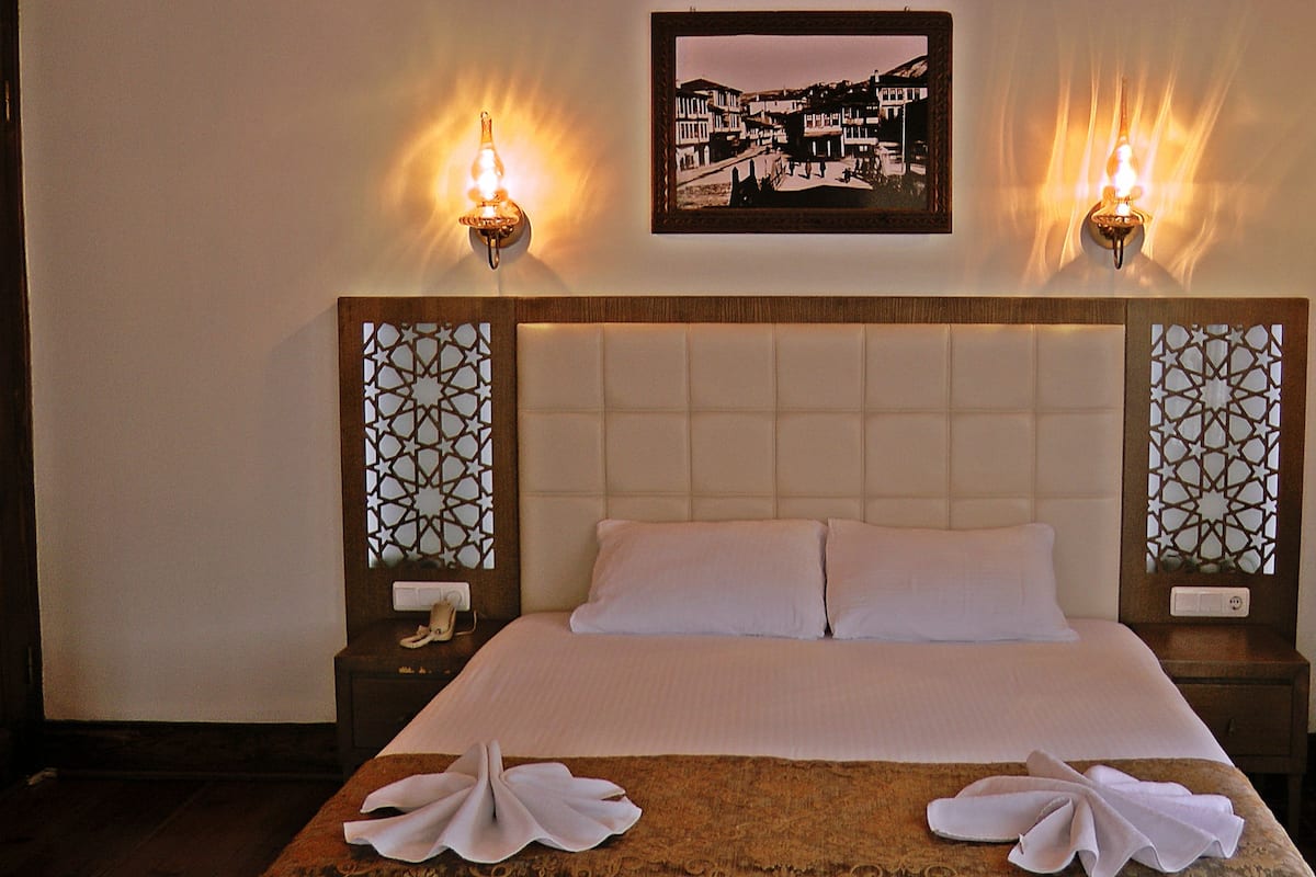 Una habitación de hotel con una cama grande, dos lámparas fijadas a la pared y un cuadro enmarcado sobre la cama.