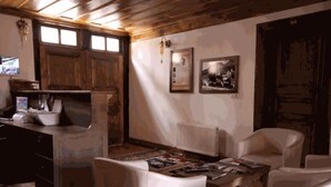 Una habitación rústica con vigas de madera, chimenea, una mesa de comedor con sillas y un radiador.