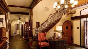 Un magnifique escalier orné de balustrades en métal ouvragé et surmonté d’un lustre, menant à une porte en bois.