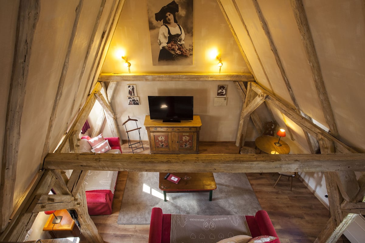 A cozy attic room with a wooden ceiling, a television, a wooden cabinet, and a red sofa.