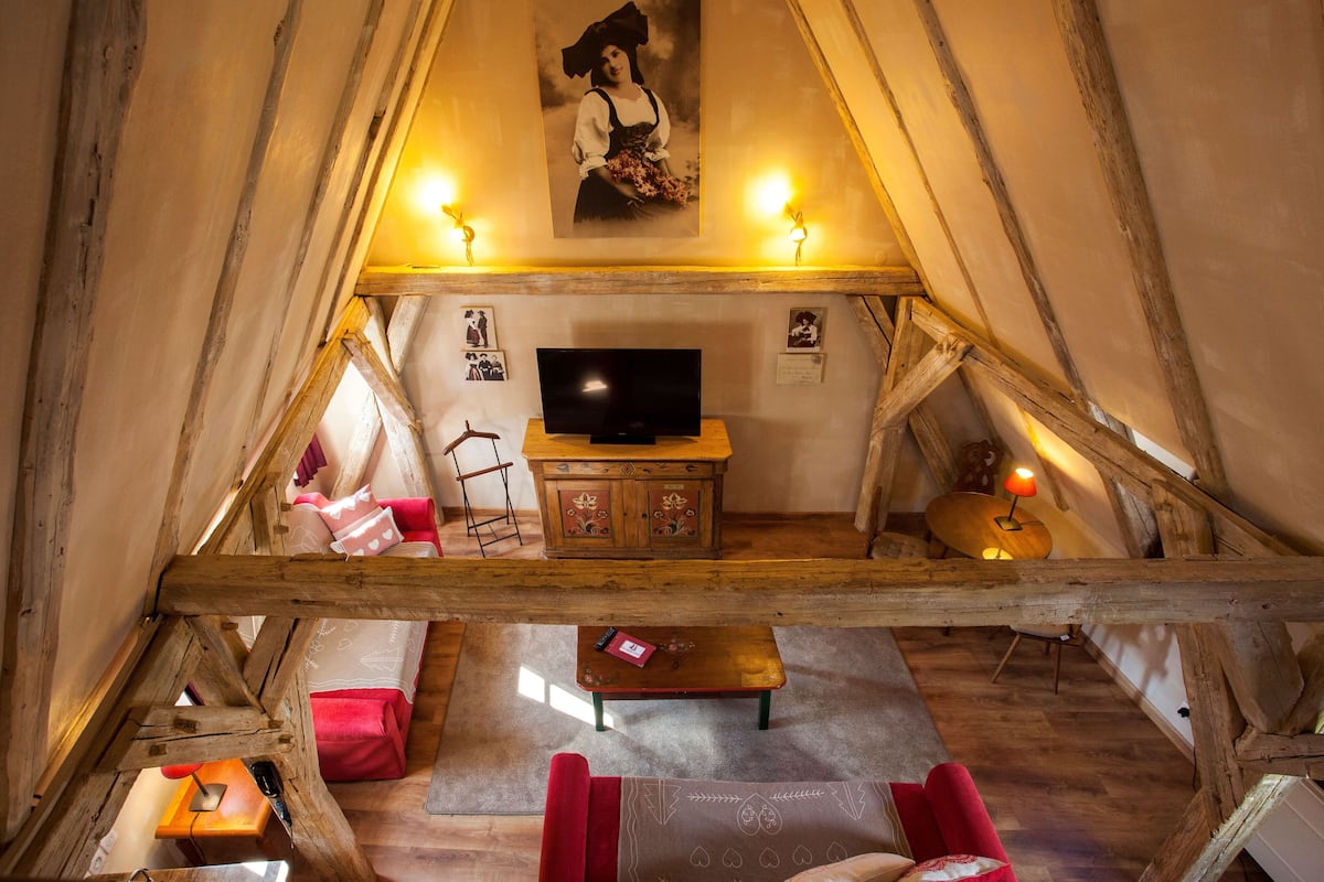 A cozy attic room with a wooden ceiling, a television, a wooden cabinet, and a red sofa.