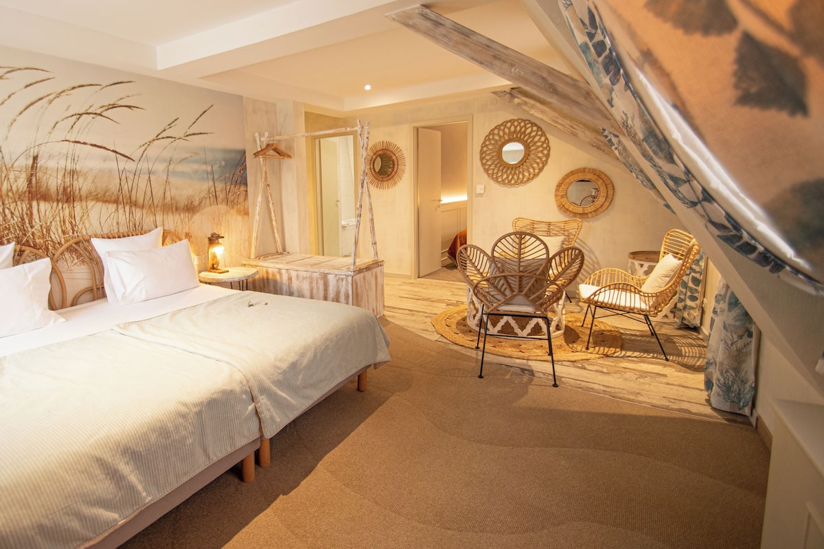 A bedroom with a large bed, two wicker chairs, and a wall mural.