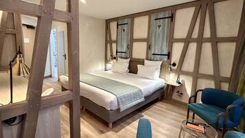A bedroom with a large bed, a wooden headboard, a bedside table with a lamp, and a blue chair.