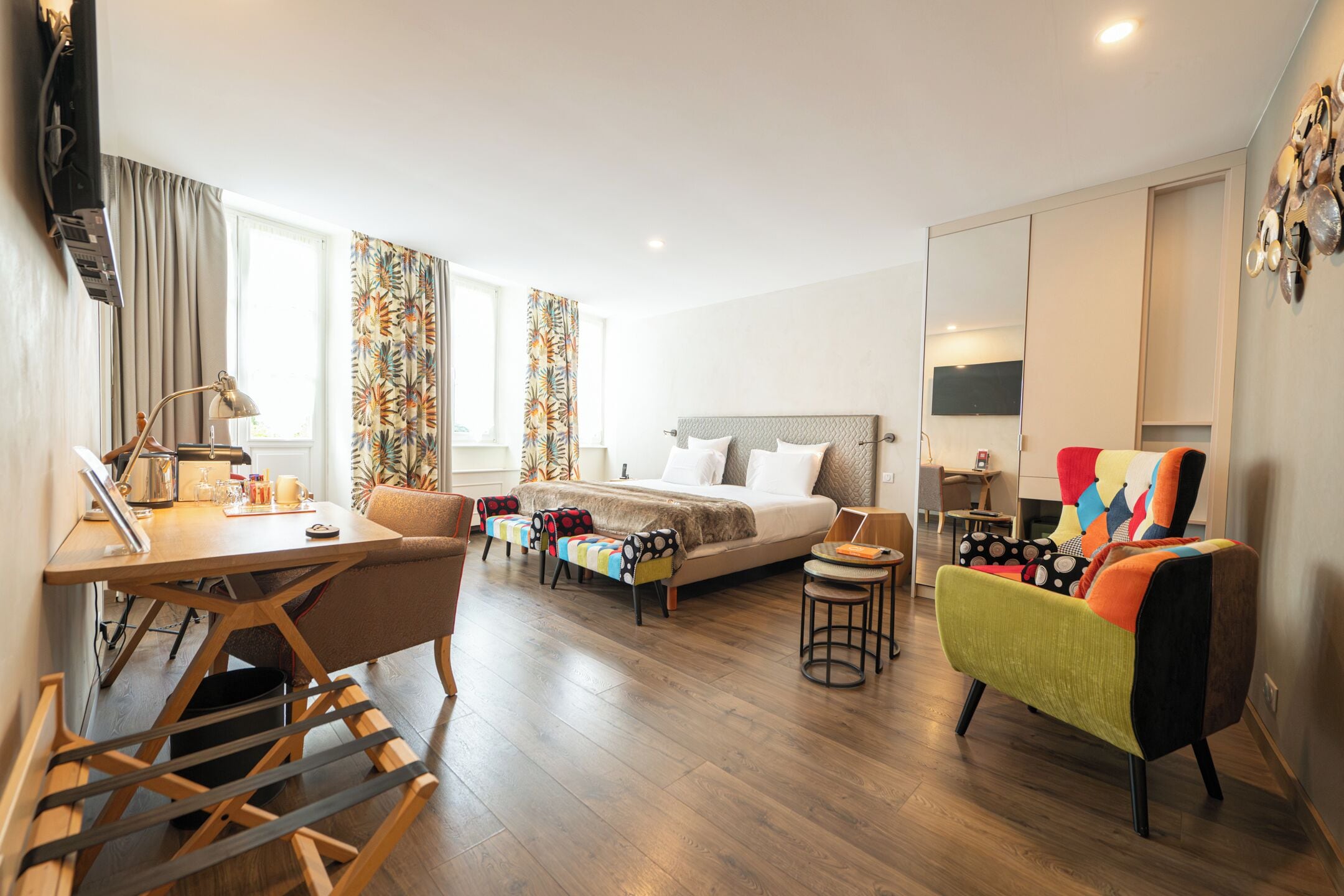 Ein modernes Hotelzimmer mit Bett, Schreibtisch, einem farbenfrohen Sessel und einem kleinen Tisch.