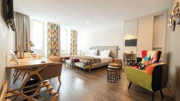 Ein modernes Hotelzimmer mit Bett, Schreibtisch, einem farbenfrohen Sessel und einem kleinen Tisch.