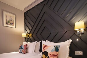 A hotel room with a modern geometric headboard, two bedside lamps, and a framed artwork on the wall.