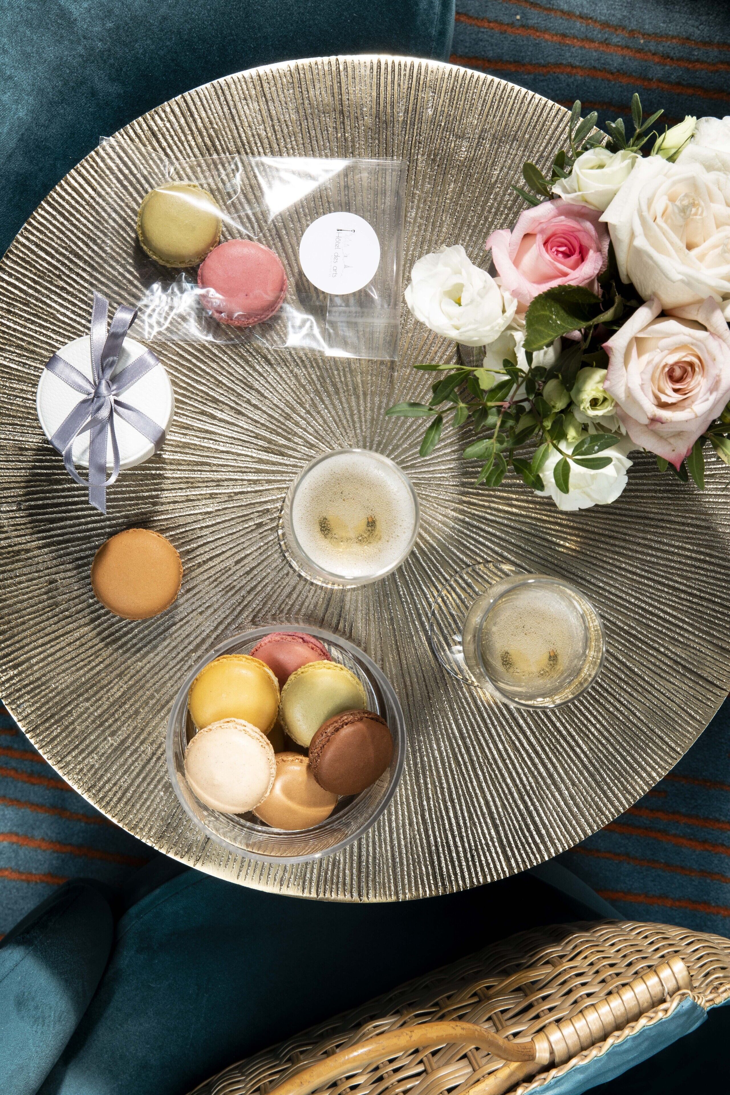 A round tray with macarons, a gift box, and a bouquet of roses on a textured surface.
