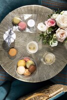 A round tray with macarons, a gift box, and a bouquet of roses on a textured surface.