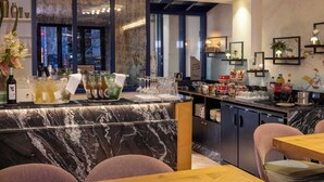 A modern bar area with marble countertops, a variety of glassware, and a selection of bottles. There are cushioned chairs and a wooden table in the foreground. - Hotel Des Arts Paris Montmartre (Paris)