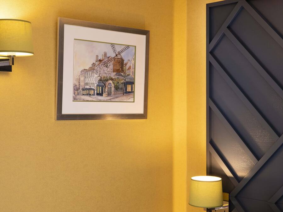 Cuadro enmarcados de una calle con edificios y un molino de viento sobre un muro amarillo.