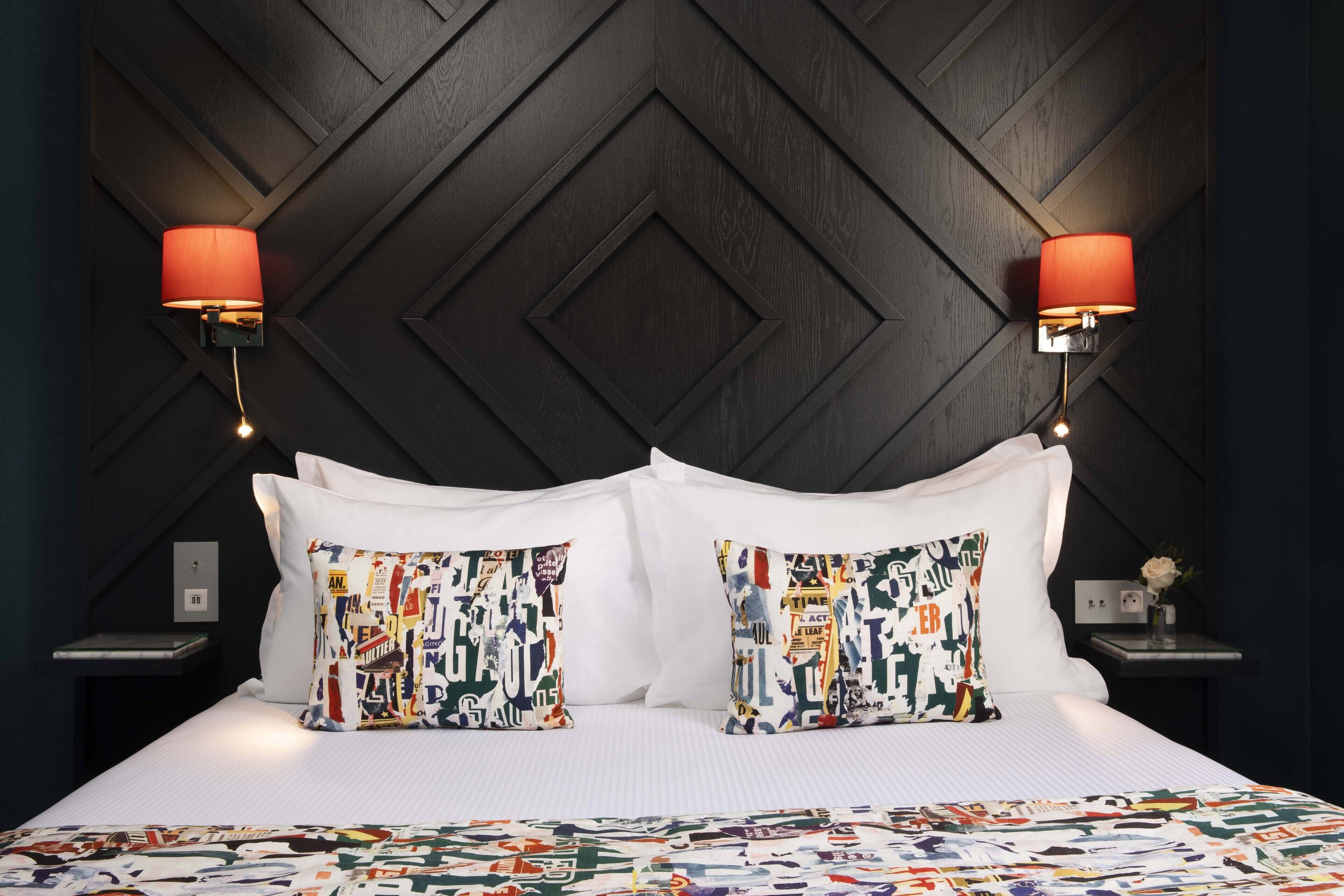 A neatly made bed with patterned pillows, a dark wooden headboard, and two wall-mounted lamps.