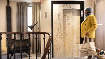 Vestíbulo de hotel con una escalera, una silla negra y una puerta con un dibujo de gato.
