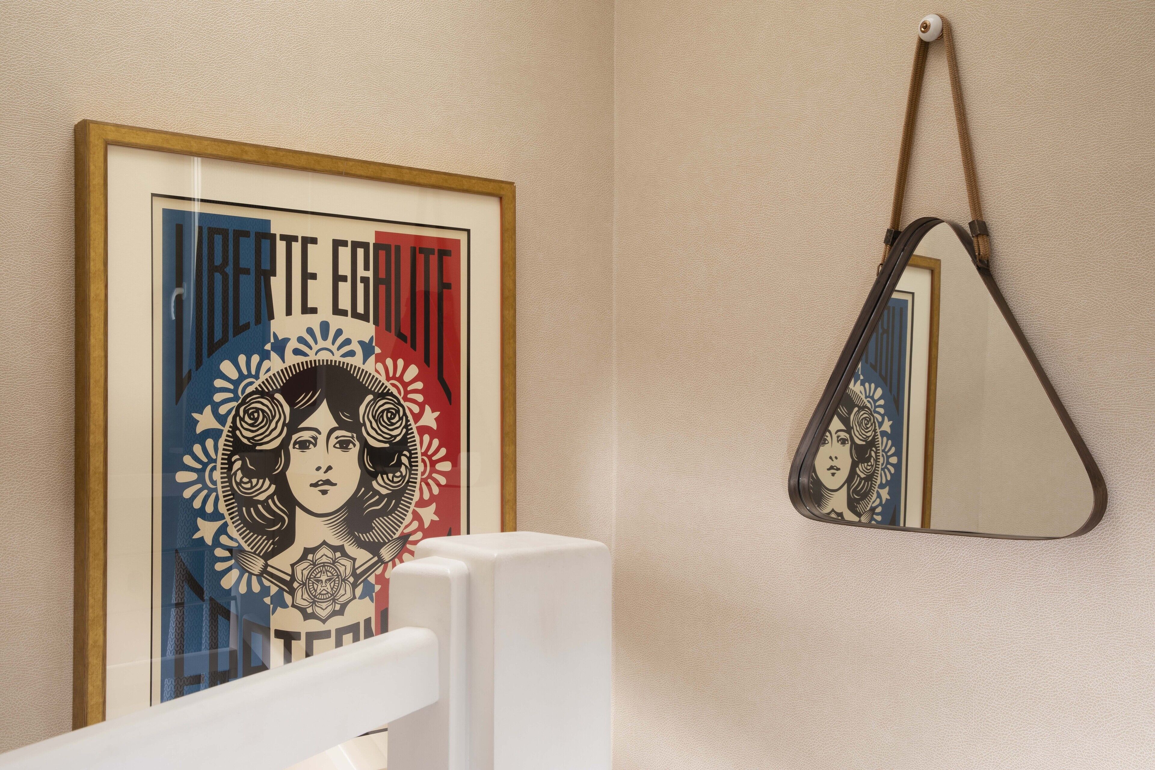 Een ingelijst poster met tekst en een bloemistisch ontwerp, een wit object op de voorgrond, en een spiegel aan de muur.