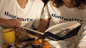 A couple reading a book with a tray of breakfast items including an apple, orange juice, and a muffin.