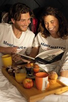 A couple reading a book with a tray of breakfast items including an apple, orange juice, and a muffin.