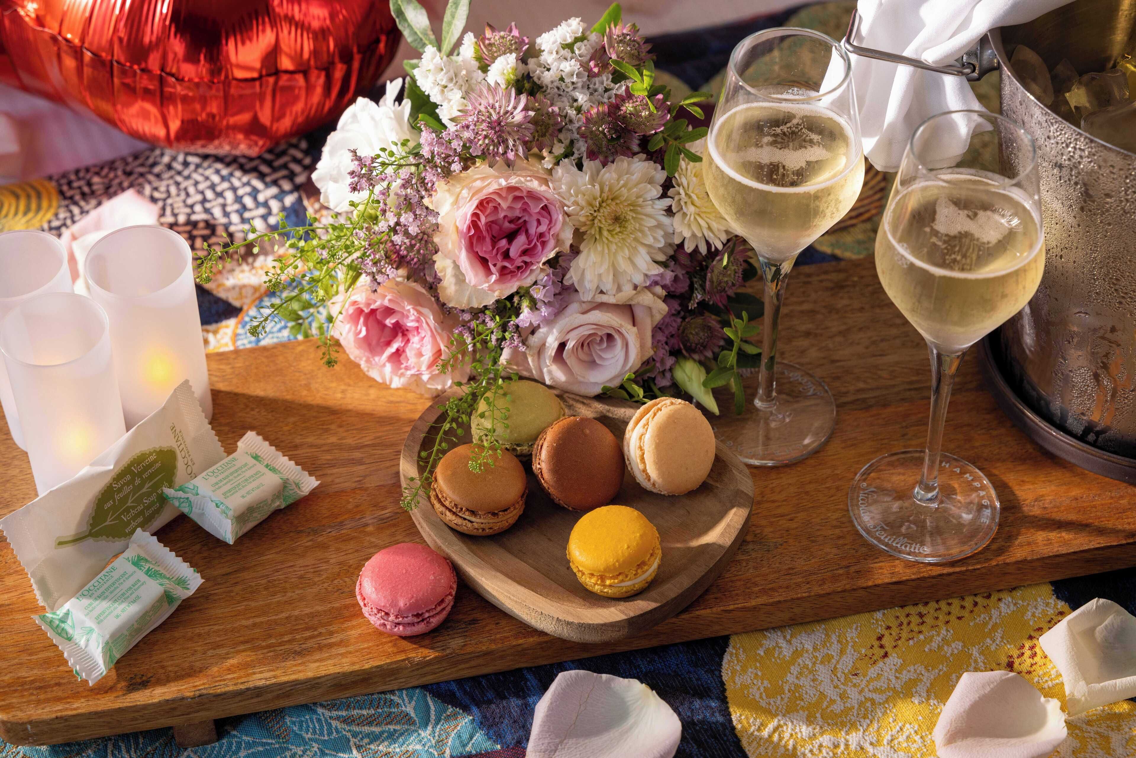 Un plateau en bois avec des macarons, un bouquet de fleurs et des verres de vin blanc.