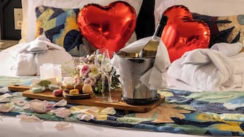 A bed with heart-shaped balloons, a champagne bottle, glasses, and a tray with snacks and flowers.