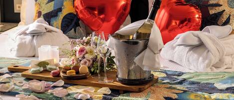Un lit décoré de ballons en forme de cœur, une bouteille de champagne, des verres et un plateau avec des amuse-gueules et des fleurs.