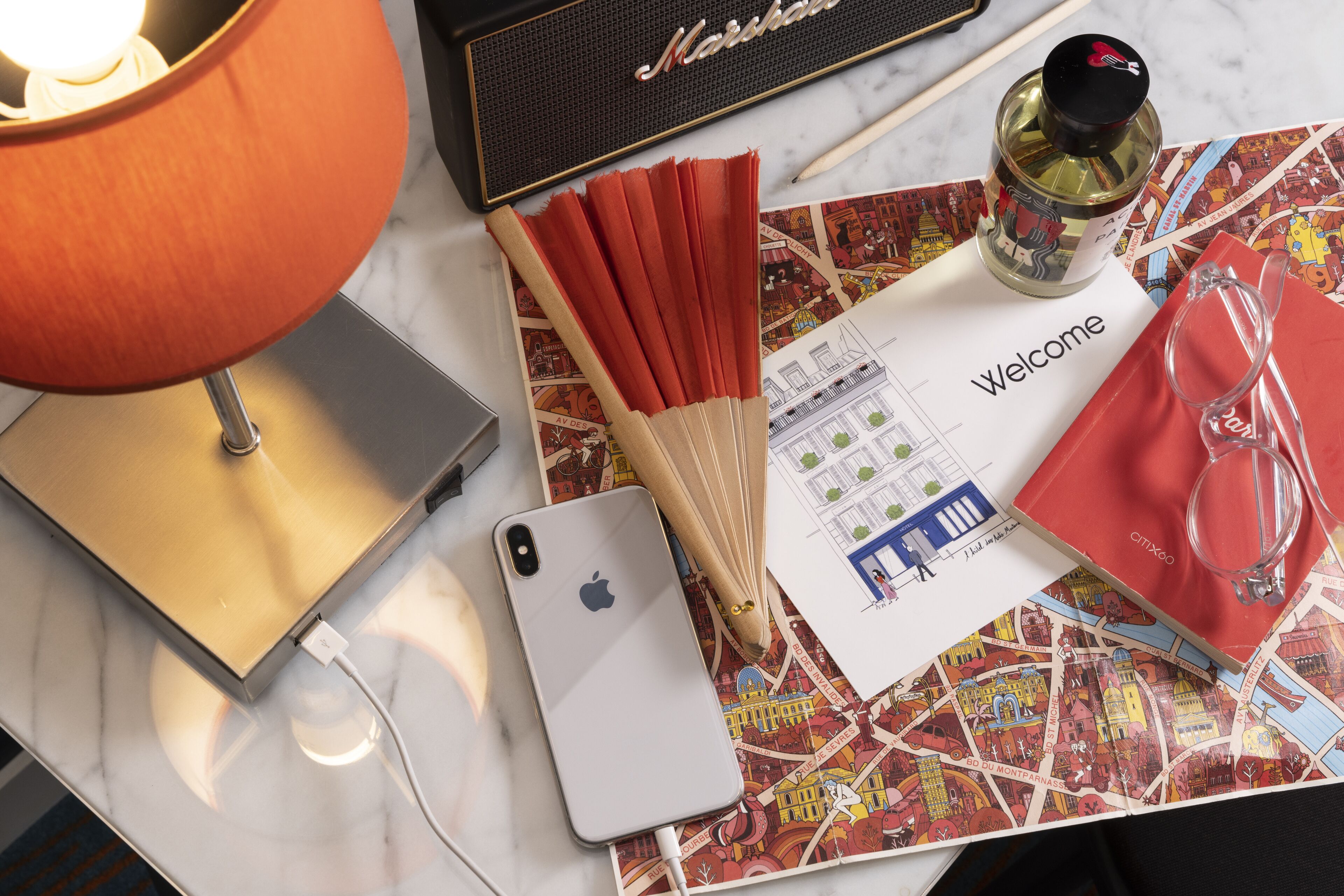A table with a lamp, a smartphone, a bottle, a pair of glasses, and a welcome card.