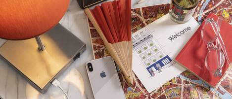 A table with a lamp, a smartphone, a bottle, a pair of glasses, and a welcome card.